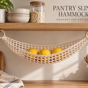 Puede incluir: Una hamaca de ganchillo beige para despensa suspendida de un estante de madera mediante dos anillos de madera clara. La hamaca contiene tres limones amarillos brillantes. El texto PANTRY SLING HAMMOCK CROCHET PDF PATTERN es visible a la derecha.