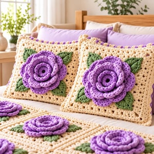 May include: Two square crochet pillows and a matching blanket featuring a cream-colored base with a large, three-dimensional purple rose in the center. Each rose is surrounded by several textured green leaves, all crafted with intricate yarn work.
