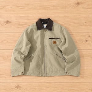 May include: A beige canvas work jacket featuring a dark brown corduroy collar, a full-length front zipper, and two slanted hand pockets. A small rectangular leather patch with the Carhartt logo is stitched onto the left chest pocket.