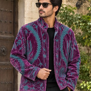 May include: A deep purple velvet jacket featuring a high collar and intricate teal green embroidery in a botanical leaf pattern. The jacket has long sleeves, a straight hem, and an open front design, worn over a plain black shirt and black trousers.