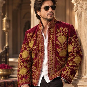 Puede incluir: Una chaqueta de terciopelo rojo intenso con intrincados bordados florales dorados en los paneles frontales y las mangas, sobre una camisa blanca de botones y pantalones negros, con gafas de sol oscuras y un reloj de pulsera metálico.