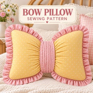 May include: A bow-shaped pillow featuring yellow fabric with white polka dots, accented by a pink ruffled border and a central pink pleated band. Above the pillow, a rectangular label displays the text BOW PILLOW SEWING PATTERN.