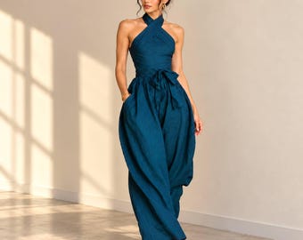 May include: A teal jumpsuit featuring a halter neckline with a crisscross bodice design. The garment includes a cinched waist with a tie-front sash and wide-leg trousers that extend to the floor, creating a fluid and structured silhouette.