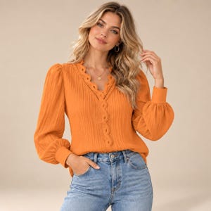 Könnte beinhalten: Eine langärmelige orangefarbene Bluse mit V-Ausschnitt, die mit einer gewellten Spitzenborte und vertikalen Falten versehen ist. Das Kleidungsstück hat Ärmel mit Bündchen und wird mit einer blauen Jeans kombiniert. Der Stoff ist durchgehend plissiert.