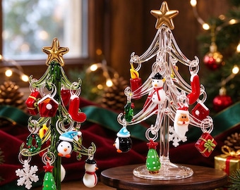May include: Two glass Christmas tree ornaments with gold stars on top. One tree is green, the other is clear. Both feature miniature hanging glass decorations including snowmen, penguins, presents, stockings, and snowflakes.