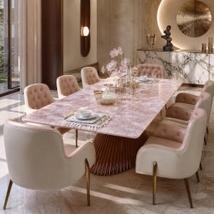Peut inclure: Une table à manger rectangulaire avec un plateau en marbre rose et une base cannelée marron foncé, entourée de huit chaises rembourrées avec des coques crème, des coussins intérieurs roses capitonnés et des pieds dorés fins.