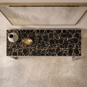 May include: A rectangular console table with a black and gold veined marble top. On the surface sits a light gray ceramic vase and a small, oval-shaped gold-toned metal bowl. The table features a sleek, metallic frame structure.