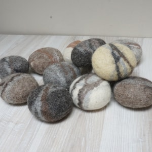 Könnte beinhalten: Eine Sammlung von zehn Filzsteinen in verschiedenen Brauntönen, Grautönen und Weiß. Die Steine sind glatt und rund und ähneln natürlichen Flusssteinen.