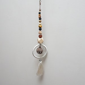 May include: A white beaded tassel hanging from a silver ring with a brown wooden ball. The beads are brown, black, and beige.