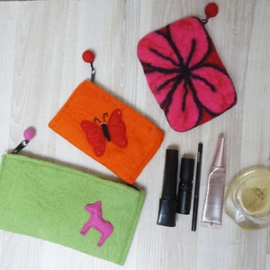 May include: Three felt zipper pouches with different designs. The first pouch is green with a pink horse design. The second pouch is orange with a red butterfly design. The third pouch is pink with a black flower design.