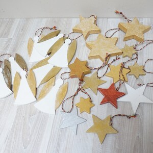 Può includere: Una collezione di addobbi natalizi in legno di varie forme, tra cui angeli e stelle. Gli addobbi sono dipinti in tonalità di bianco, oro e rame.