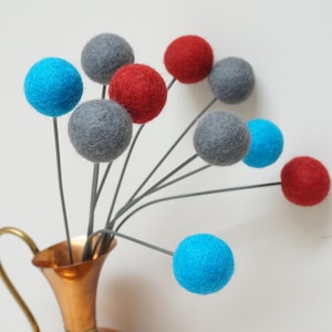 May include: A copper vase with a gold handle holds a bouquet of felt balls. The balls are in shades of grey, blue, and red.