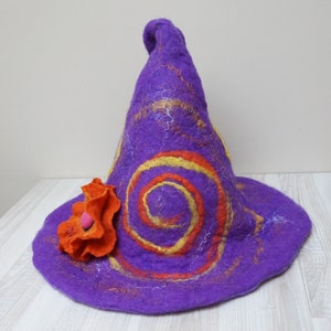 Op de afbeelding: Paarse vilten tovenaarhoed met oranje en gele swirls en een grote oranje vilten bloem.