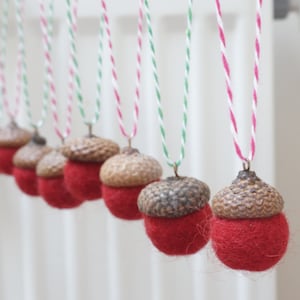 Könnte beinhalten: Eine Reihe von Eichel-Anhängern mit roten Filz-Böden und braunen Eichel-Deckeln, die an einer Schnur mit roten und weißen Streifen hängen.