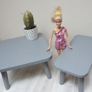 Può includere: Due mobili in legno grigi per case di bambole, un tavolo quadrato e una panca rettangolare, con un piccolo cactus in vaso sul tavolo.