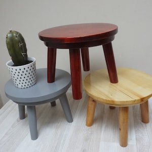 May include: Three wooden stools, one painted gray, one painted red, and one natural wood. The stools are all round and have three legs. A potted cactus sits on top of the gray stool.