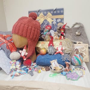 Puede incluir: Una colección de artículos navideños que incluye un gorro de punto color óxido con orejeras y un pompón sobre una cabeza de madera, tela de punto azul, bolas de lana fieltrada, pequeñas figuras de gnomos, un bolso de fieltro y adornos.