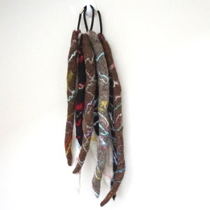 May include: A set of five brown wool dreadlocks with colorful embroidery. The dreadlocks are tied together with a black elastic band.