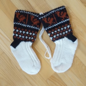 Könnte beinhalten: Ein Paar weiße Stricksocken mit braunen und schwarzen gemusterten Bündchen. Die Bündchen haben ein geometrisches Muster mit kleinen braunen Vögeln.