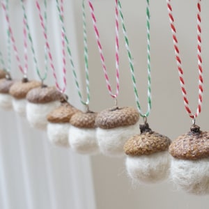 Könnte beinhalten: Eine Reihe von Eichel-Anhängern mit weißem Filz, der die untere Hälfte jeder Eichel bedeckt. Die Eicheln sind an rotem und weißem Garn sowie an grünem und weißem Garn aufgefädelt.