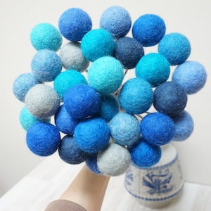 May include: A bouquet of blue and turquoise felt balls on a white background. The balls are arranged in a gradient from dark blue to light blue.