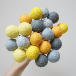 May include: A bouquet of felt balls in shades of yellow, orange, and grey. The balls are arranged in a cluster and are attached to thin wires.