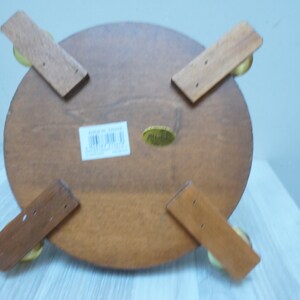 May include: The bottom of a wooden round table with four legs. The legs are attached to the table with brass screws. The table has a label on the bottom that says "Made in China".