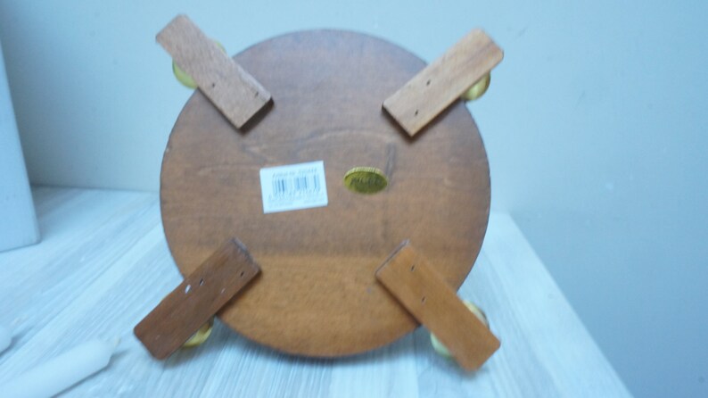 May include: The bottom of a wooden round table with four legs. The legs are attached to the table with brass screws. The table has a label on the bottom that says "Made in China".