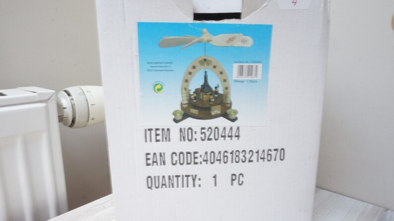 May include: A white cardboard box with a picture of a wooden Christmas pyramid with a star on top. The box has the text "ITEM NO: 520444", "EAN CODE: 4046183214670", and "QUANTITY: 1 PC" printed on it.