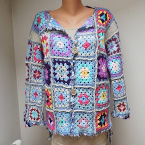 Puede incluir: Una chaqueta de punto azul de ganchillo con un diseño de patchwork colorido. La chaqueta tiene cuello en V y cierre de botón.