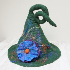 Op de afbeelding: Een groene vilten toverhoed met een gekrulde rand en een blauwe bloem met een oranje hart.