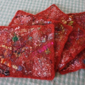 May include: A set of four red felt coasters with intricate embroidery in various colours, including pink, blue, and green. The coasters are layered on top of each other, showcasing the detailed design.