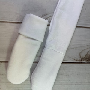 May include: A pair of white fleece mittens, one shorter with a folded cuff and one longer with an extended forearm section. Both mittens feature a rounded thumb-less design and a soft, matte texture, crafted from a solid white fabric throughout.