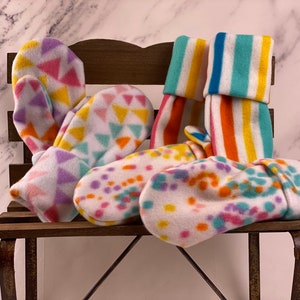 May include: A set of colorful fleece mittens and socks. The mittens have a geometric pattern in shades of pink, yellow, and purple. The socks have stripes in shades of yellow, orange, and turquoise.