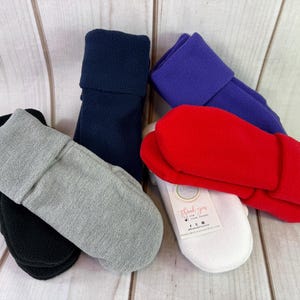 Puede incluir: Una colección de manoplas de forro polar en varios colores sólidos, incluyendo negro, gris, azul marino, morado, rojo y blanco. La manopla blanca presenta una pequeña etiqueta rectangular con el texto Thank you for your order y un icono.