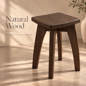 May include: A dark walnut finished wooden stool with a square seat and four slightly angled legs. The text Natural Wood and Finished in Dark Walnut is visible on the left side of the stool, which features a visible wood grain texture.