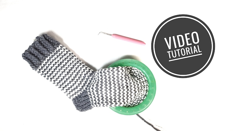 May include: A gray and white striped crocheted sock with a green yarn bowl and a pink crochet hook. The image includes the text "VIDEO TUTORIAL".
