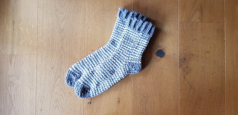 May include: A gray and white striped knitted sock with a folded cuff.