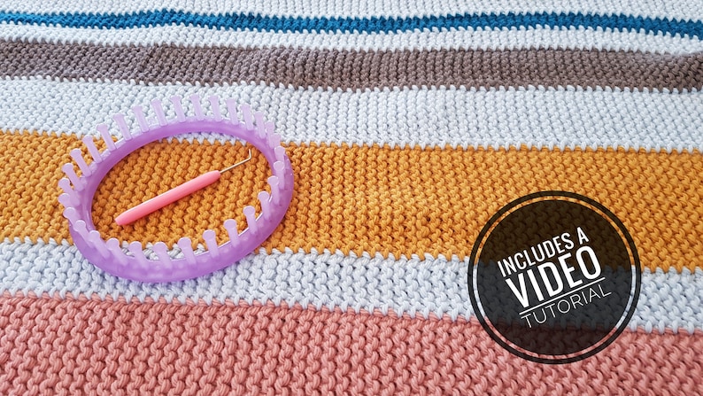 May include: A lavender knitting loom and pink crochet hook rest on a colorful knitted blanket. The blanket features horizontal stripes in shades of blue, brown, white, yellow, and pink. A circular graphic states "INCLUDES A VIDEO TUTORIAL".