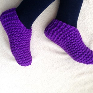 May include: Purple knitted slipper socks. The socks are made with a simple stitch pattern and have a soft, cozy look.