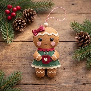 May include: A felt gingerbread person ornament featuring a red and white polka dot bow, a green dress with a white scalloped hem, and a red mug with a white heart. The figure has black bead eyes, pink cheeks, and a red and white string loop.