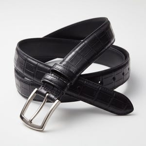Puede incluir: Un cinturón negro con un patrón de relieve de cocodrilo en toda la correa. El cinturón incluye una hebilla de metal plateado pulido con una sola púa y una trabilla a juego, enrollado para mostrar el detalle de la correa y la hebilla.