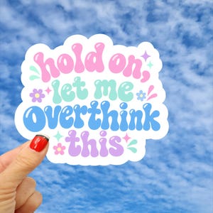 May include: A die-cut sticker featuring the text "hold on, let me Overthink this" in a bubbly, rounded font. The words are colored in pink, light blue, and purple, accented with small decorative stars and flowers in matching pastel shades.