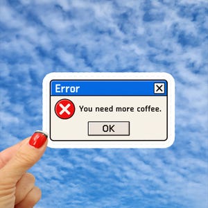 May include: A rectangular sticker featuring a retro computer error message box with a blue title bar, a red circular icon with a white X, the text "Error" and "You need more coffee.", and a gray "OK" button on a light beige background.