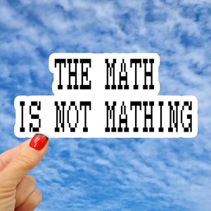 May include: A white die-cut sticker with a black pixelated font that reads THE MATH IS NOT MATHING. The sticker has a clean white border around the text, creating a sharp contrast against the background.