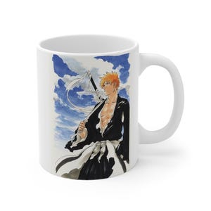 Peut inclure: Un mug en céramique blanche orné d'une illustration imprimée représentant un personnage d'anime aux cheveux orange en bataille, vêtu d'une tenue noire et blanche avec une épée dans le dos, sur un fond de ciel bleu avec des nuages blancs.
