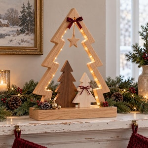May include: A light-colored wooden Christmas tree frame with integrated warm LED lights, featuring a dark brown wooden tree and a light wooden tree inside. A small wooden star hangs from a dark red velvet bow at the top.