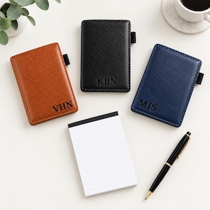 May include: Three rectangular pocket notebooks with covers in tan, black, and navy blue, each featuring a black elastic pen loop and embossed initials VHN, KBN, or MJS. A white lined notepad and a black and gold ballpoint pen are included.
