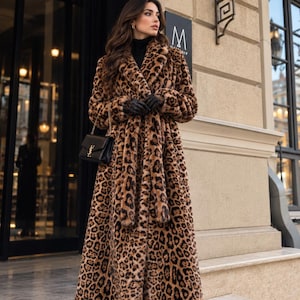 May include: A long, floor-length coat featuring a brown and black leopard print pattern with a wide collar, long sleeves, and a matching tie belt. The coat is worn over a black turtleneck, paired with black leather gloves and black boots.