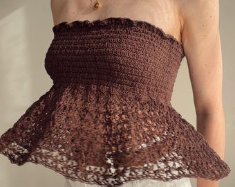May include: A dark brown strapless crochet top featuring a fitted, ribbed bodice with a ruffled top edge and a flared, open-work lace peplum hem. The garment is crafted with a textured yarn pattern and has a distinct transition between the tight knit bodice and the loose, airy crochet skirt section.